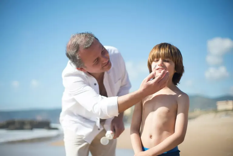 Ojciec aplikujący filtr przeciwsłoneczny dziecku na plaży